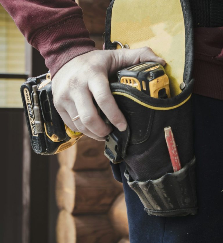 Hand hält Werkzeugtasche mit verschiedenen Werkzeugen und einem Maßband.