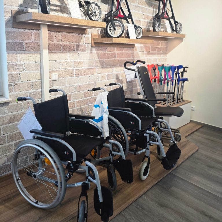 Reha Hilfsmittel Orthopädietechnik Schröter Zwei Rollstühle und mehrere Gehhilfen auf einem Holzregal in einem Innenraum.