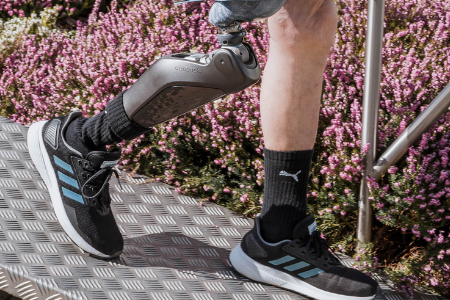 Bein mit Prothese in einem sportlichen Schuh, umgeben von blühenden Pflanzen.