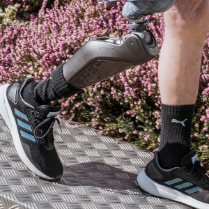 Ein Mann mit einer Prothese und Sneakers mit blauen Streifen steht auf einem Pflaster.