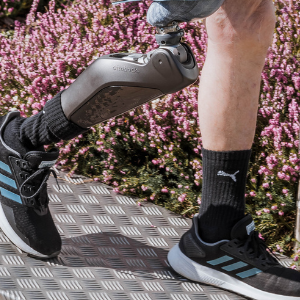 Person mit Beinprothese trägt sportliche Schuhe und schwarze Socken, umgeben von Blumen.