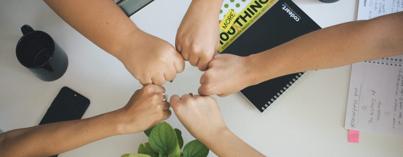 Fünf Hände geben sich einander fist bumps auf einem Tisch mit Büromaterialien.